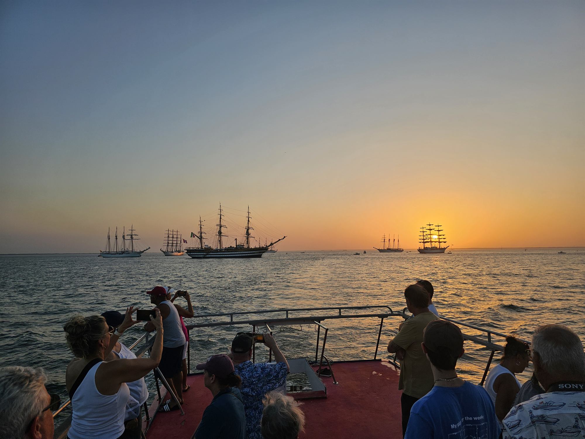 Guests watching tall ships at sunset from the deck